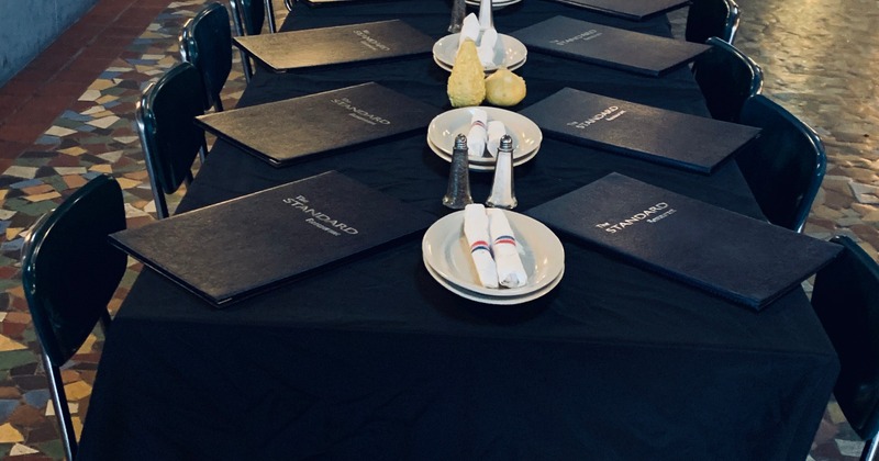 A long table covered with a dark cloth, set with plates, utensils, and menus