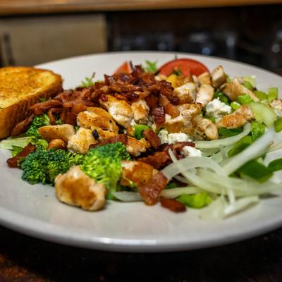 Grilled chicken salad topped with bacon bites and served with toast.
