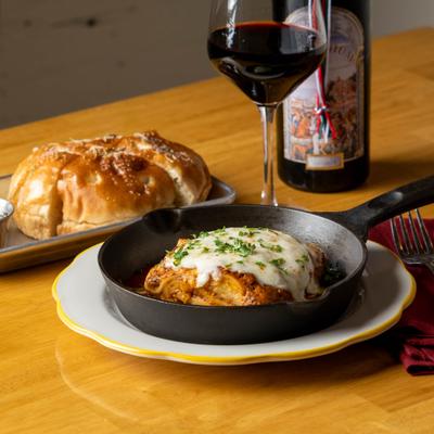 Lasagna topped with melted cheese, accompanied by red wine and focaccia.