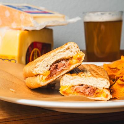 Grilled cheese sandwich and chips, with cheese and beer in the background.