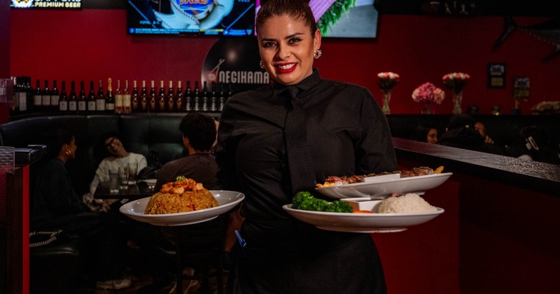 Smiling server in black uniform holds food plates in the restaurant