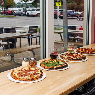 Several pizzas arranged in a row on a wooden counter next to a large window.