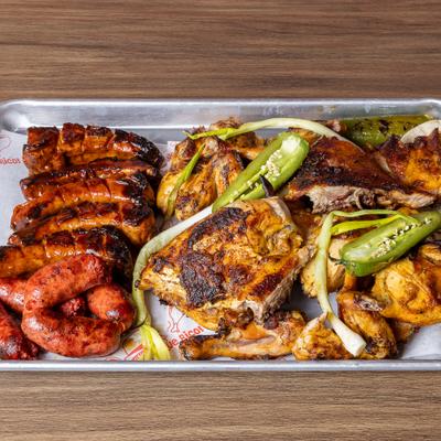 Combination grill platter featuring variety of meats served on a paper lined tray.