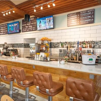 Bar area with leather stools. TVs, menu boards, and shelves of liquor