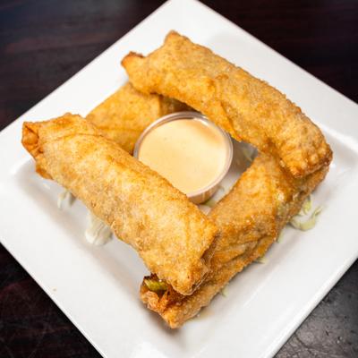 Plate of crispy fried pickle egg rolls served with a cup of creamy sauce.
