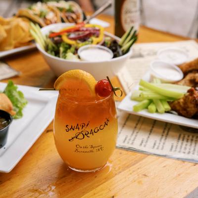 Orange-layered drink topped with citrus and a cherry, served alongside various dishes.