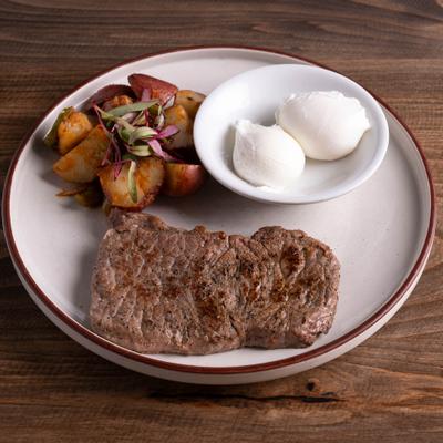 A grilled steak and two poached eggs served with roasted potatoes.