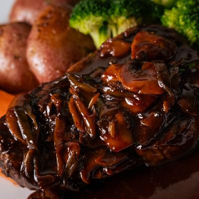 Close-up of a steak smothered in dark mushroom gravy, served with broccoli and potatoes.