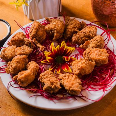 Plate of hot spicy chicken garnished with a flower and served with a dip.