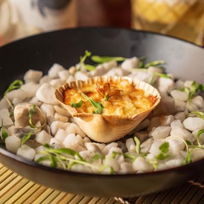 Nikkei scallops served in a scallop shell on a bed of white stones.