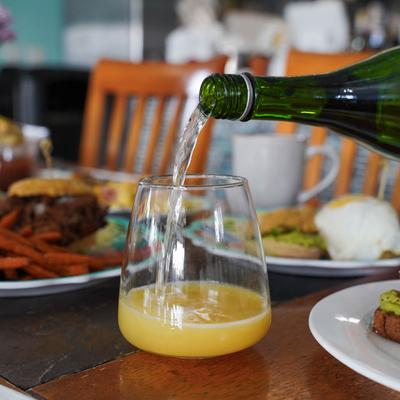 Sparkling wine being poured into a glass of orange juice on a table with plated food.
