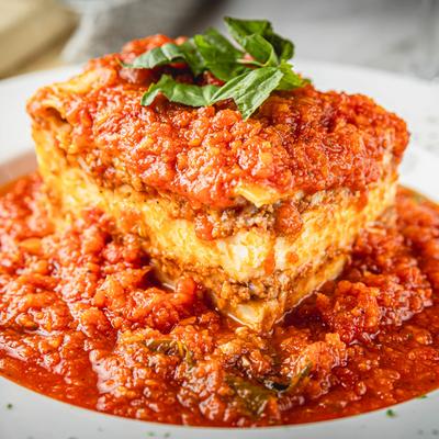A slice of lasagna in tomato sauce topped with basil.