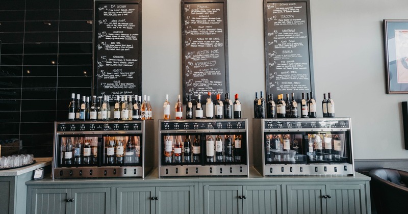 A modern wine display - dispensers with various wine bottles, flanked by chalkboard menus.