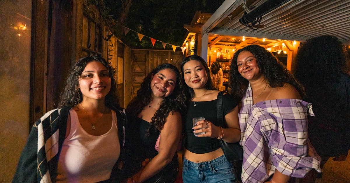 Four patrons smiling and posing at Pastiche at a nighttime outdoor gathering