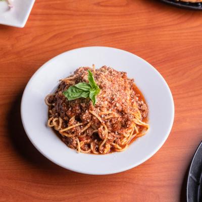 Plate of meat sauce spaghetti, topped with cheese and a fresh basil garnish.