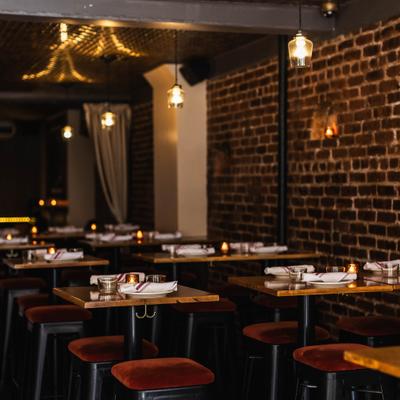 High-top wooden tables set for dining, plush red stools, and an exposed brick wall.
