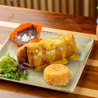 Chimichanga topped with cheese sauce served with rice, refried beans, and guacamole.