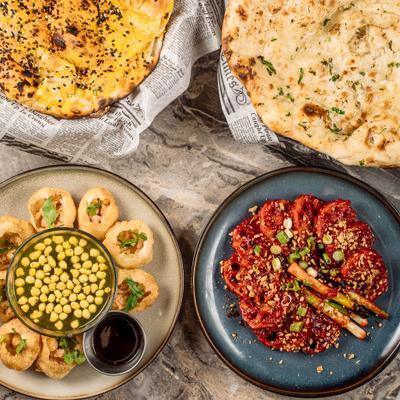 Pani Puri, chili chicken, garlic and plain naan served on a table, overhead view.