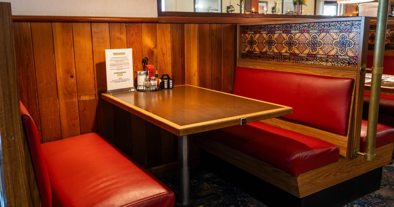 A cozy dining booth in a restaurant with red seating, a brown table