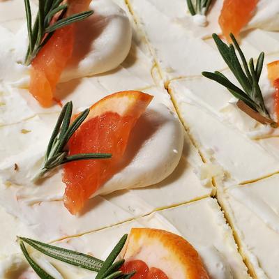 Cake slices with white icing, garnished with red grapefruit slices and rosemary leaves.