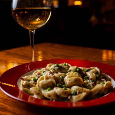 Cheese tortellini pasta in creamy sauce with peas, herbs, and a glass of white wine.