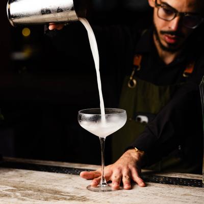 Bartender pouring a cocktail into a martini glass.