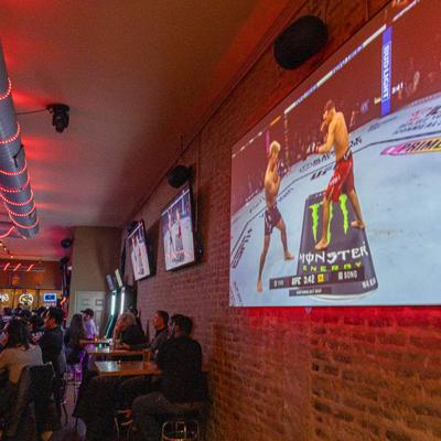 Interior, crowd in seating area with large TVs on brick wall.