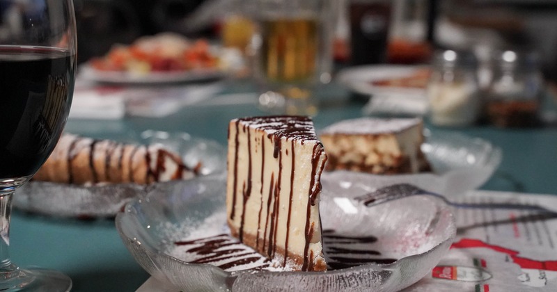 Slice of cheesecake with powdered sugar and chocolate drizzle served on a glass plate
