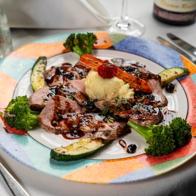 Grilled Sliced Breast of Duck with sauce, mashed potatoes, and vegetables on a colorful plate.