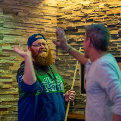 Two patrons are high-fiving near a lit fireplace with a stone wall background.