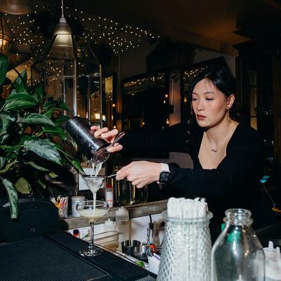 A bartender straining a cocktail into a glass.
