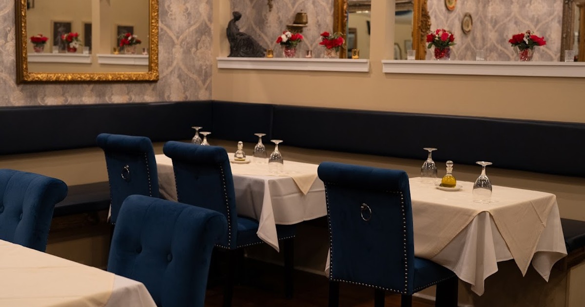 Elegant restaurant interior with beige walls, blue velvet chairs, and tables set with ivory linens