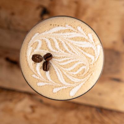 Overhead view of an espresso martini cocktail with coffee bean garnish and intricate foam art.