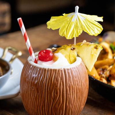Pina Colada served in a coconut tiki mug with cherry, pineapple, and umbrella garnish.