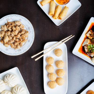 Asian food spread with sesame balls, steamed buns, fried chicken bites, and spring rolls.