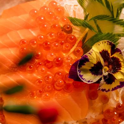 Close-up of a Japanese rice bowl with raw salmon, roe, and flower garnish.