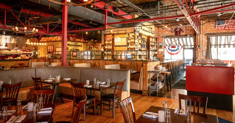 Interior of a restaurant with wooden tables, booths, a bar, and warm lighting