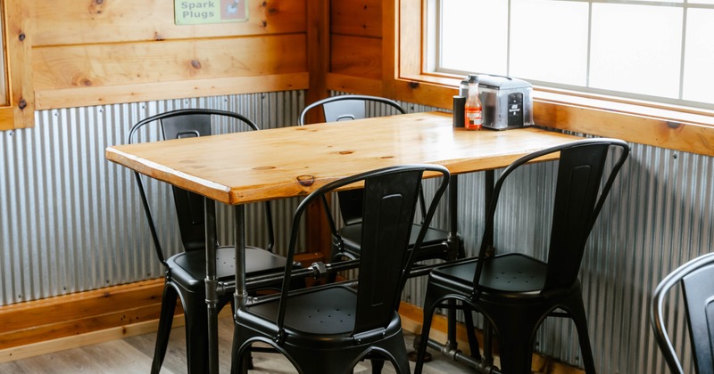 A wooden dining table with black metal chairs; wood and corrugated metal walls
