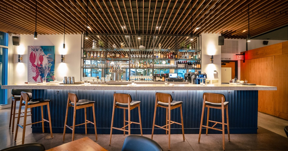 Modern bar interior with wooden ceiling slats, a stone counter, and bar stools