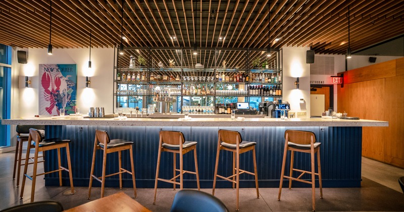 Modern bar interior with wooden ceiling slats, a stone counter, and bar stools