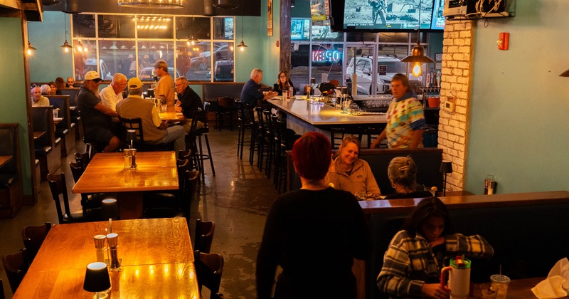 Interior with wooden tables, a bar, and television screens