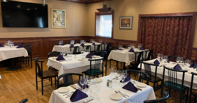 Dining tables covered with white table cloths, with tableware, cutlery and wine glasses