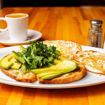 Avocado on toasted bread with fried eggs and a cup of coffee.