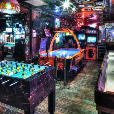 Retro arcade with neon lights, featuring air hockey, foosball, and vintage arcade games