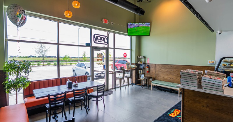 A modern pizzeria interior - large windows; a table with black chairs.