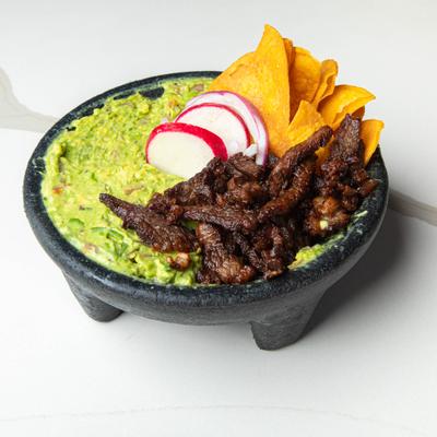 Fried slices of ribeye steak placed on top of fresh guacamole with tortilla chips.