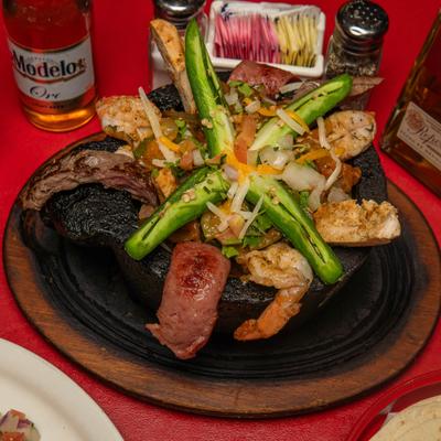 Mixed molcajete with steak, shrimp, and chicken, served in a traditional stone bowl with a beer.