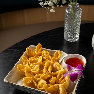 Crab rangoon plate on a black table with a vase of little white flowers.