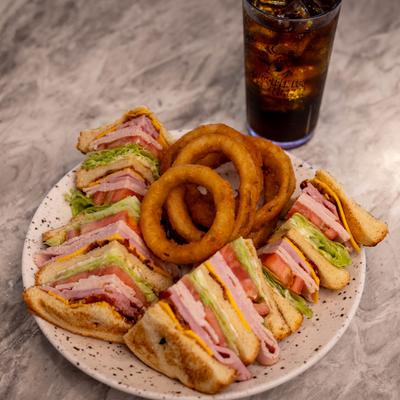 Club sandwich with a side of onion rings and a soft drink.
