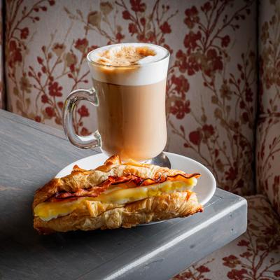 Bacon. egg, and cheese croissant sandwich served with a cup of latte.